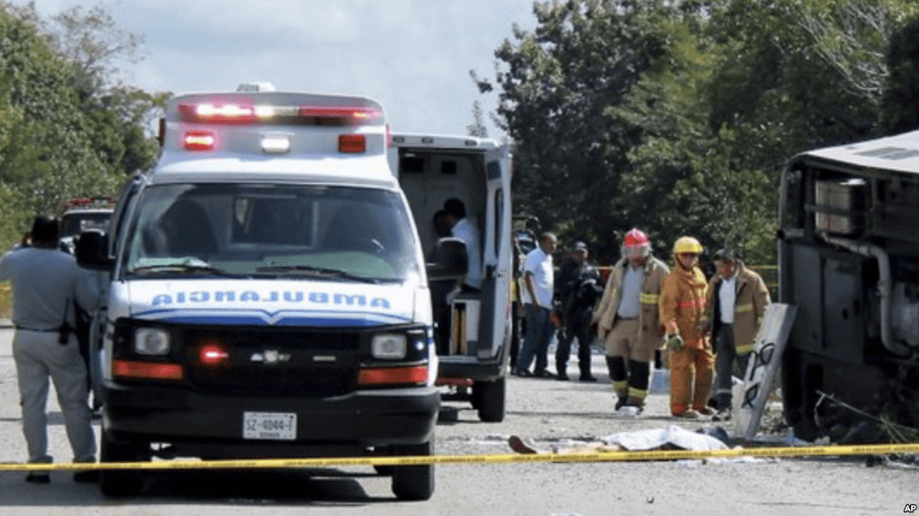 El cuerpo sin vida de un pasajero se encuentra al lado de un autobús volcado, mientras ambulancias, bomberos y policías, se encuentran en Mahahual, estado de Quintana Roo, México, el martes 19 de diciembre de 2017.
